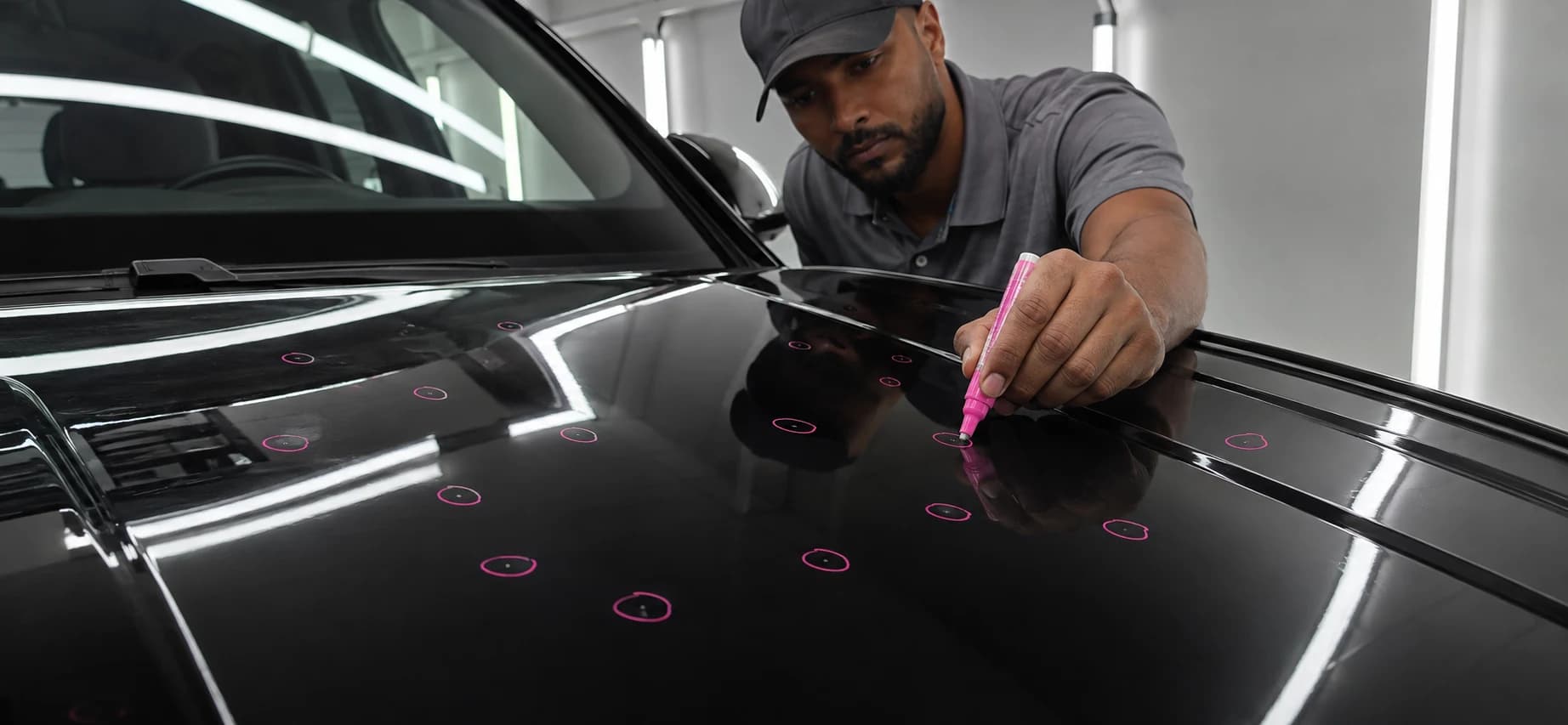 AI illustration of a technician carefully circling hail dents on a black hood